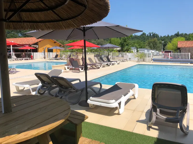 Piscine et transats sous les parasols au Camping des Sources